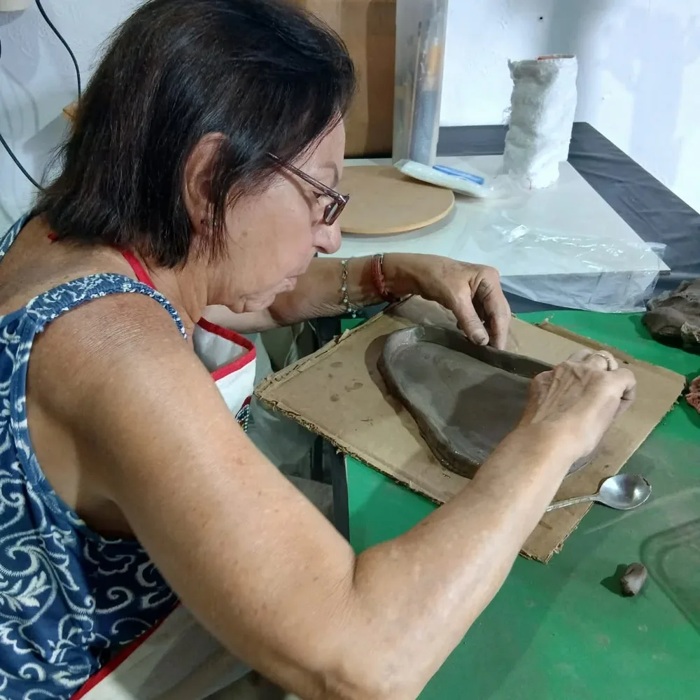 Aluna modelando uma peça de argila sobre a mesa da oficina da PEBOZ